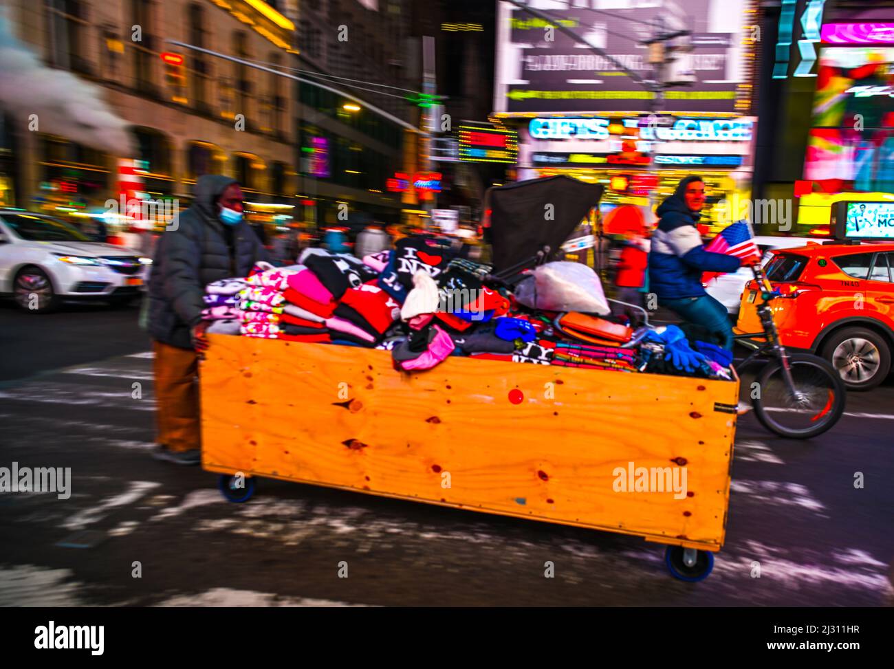 Homme avec sa boîte de marchandises à vendre en le poussant vers le bas 42nd Street à Manhattan avec la circulation et un homme sur un bicycle Banque D'Images