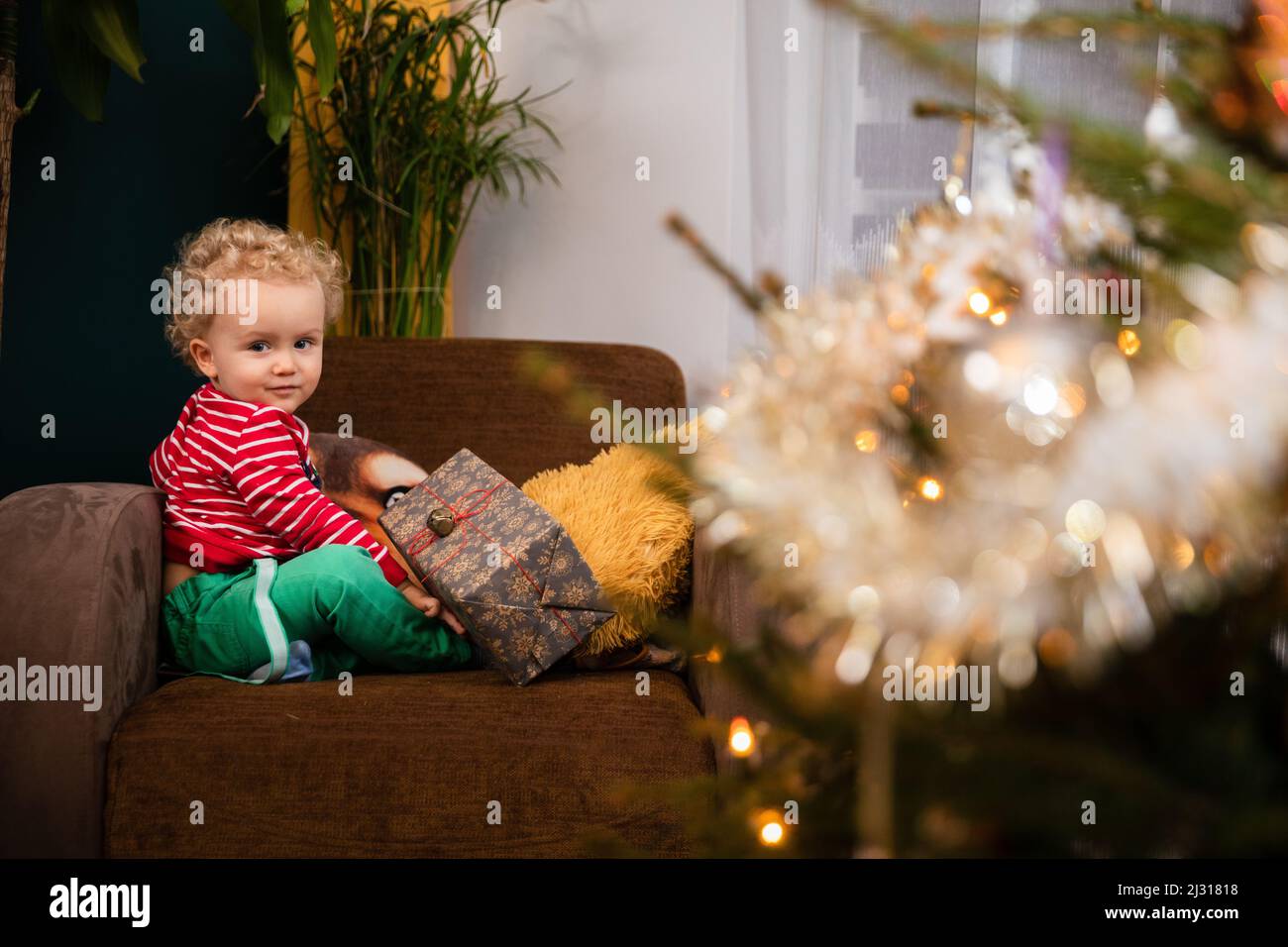 Un petit garçon s'assoit sur une chaise avec un cadeau et des sourires. Banque D'Images