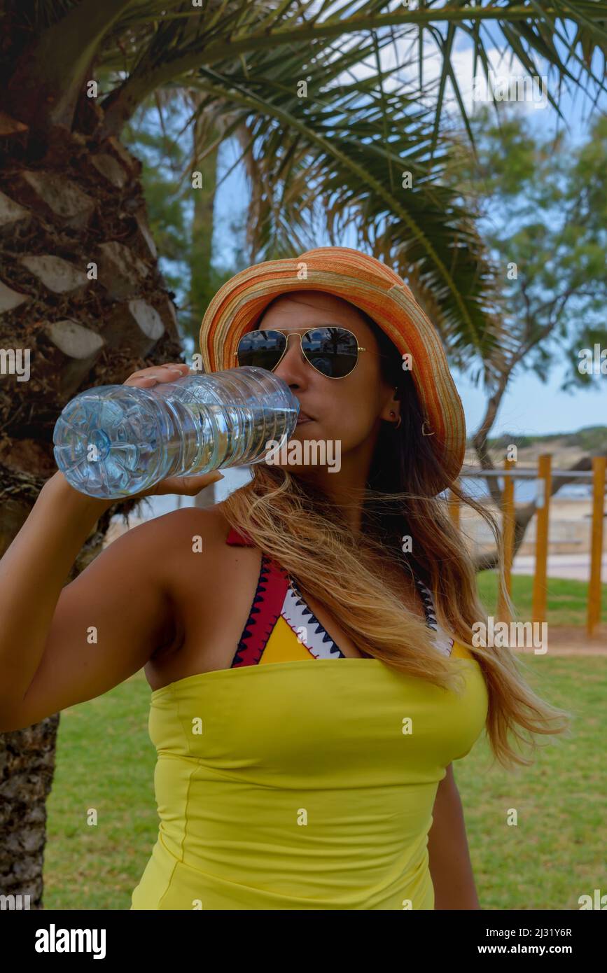 Bonne femme qui boit de l'eau minérale à côté d'un palmier en profitant de l'été. CopySpace. Banque D'Images