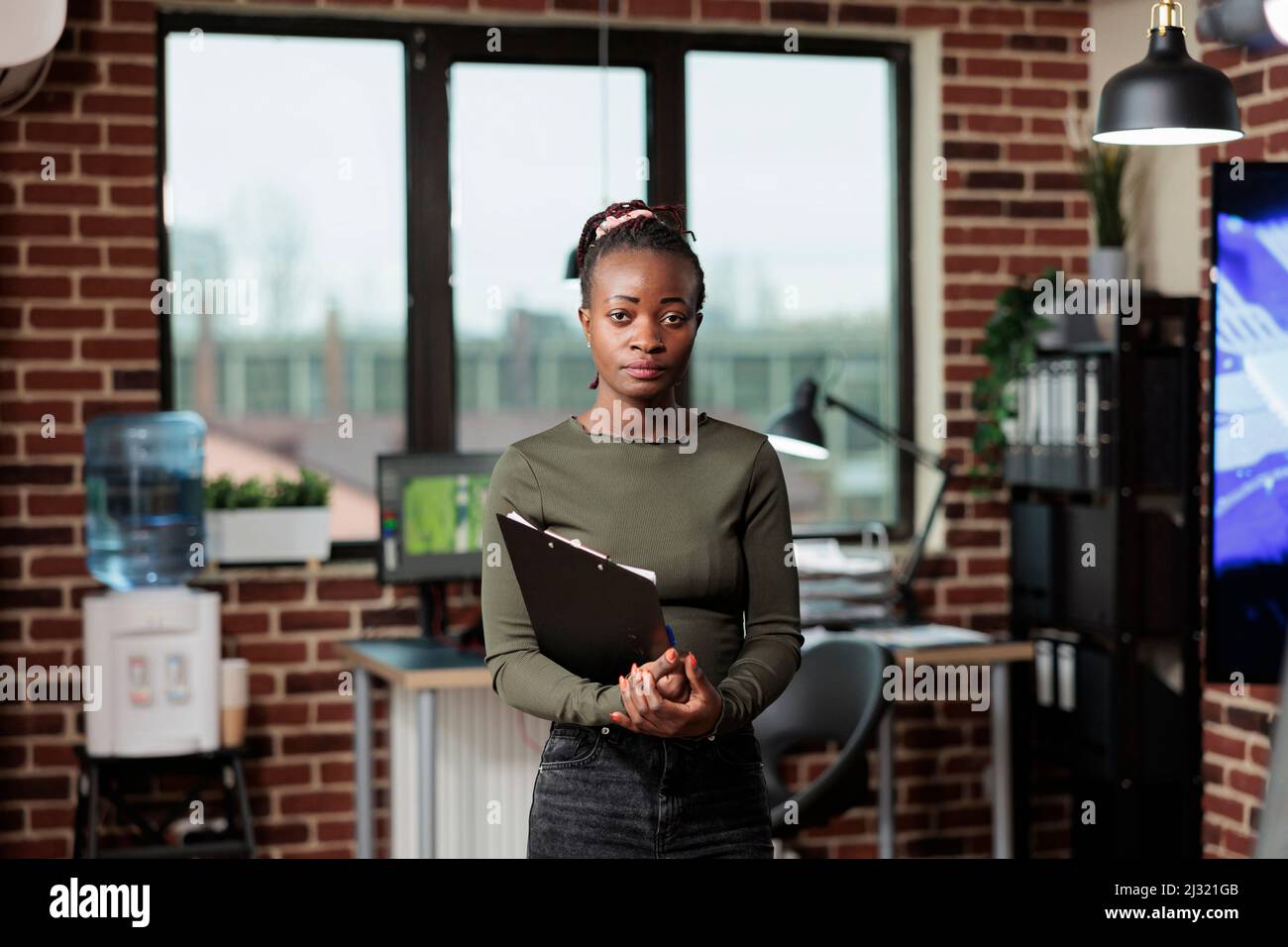 Entreprise créative jeune artiste numérique avec un bloc-notes de gestion dans un espace de travail de bureau. Créateur artistique professionnel de l'agence disposant de la documentation du plan de production tout en regardant la caméra. Banque D'Images