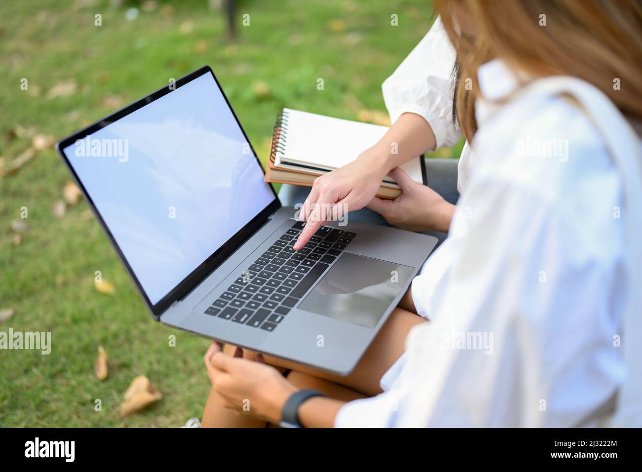 En gros plan, une étudiante d'université féminine utilisant un ordinateur portable pour travailler son travail avec son ami dans Green Park. Banque D'Images