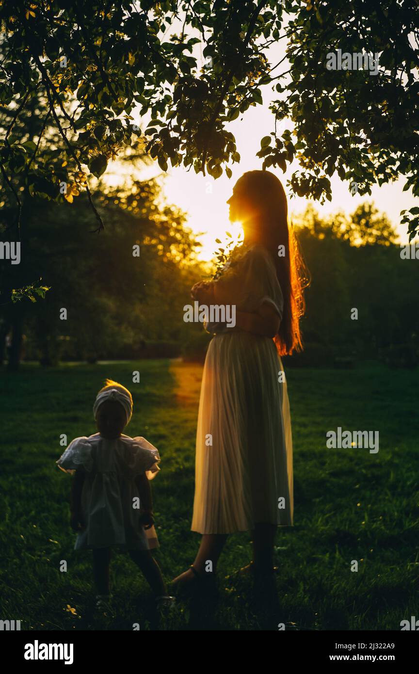 Mère et petite fille dans lumière du coucher du soleil, concept de printemps. Vue de profil, avec effet de flou. Banque D'Images