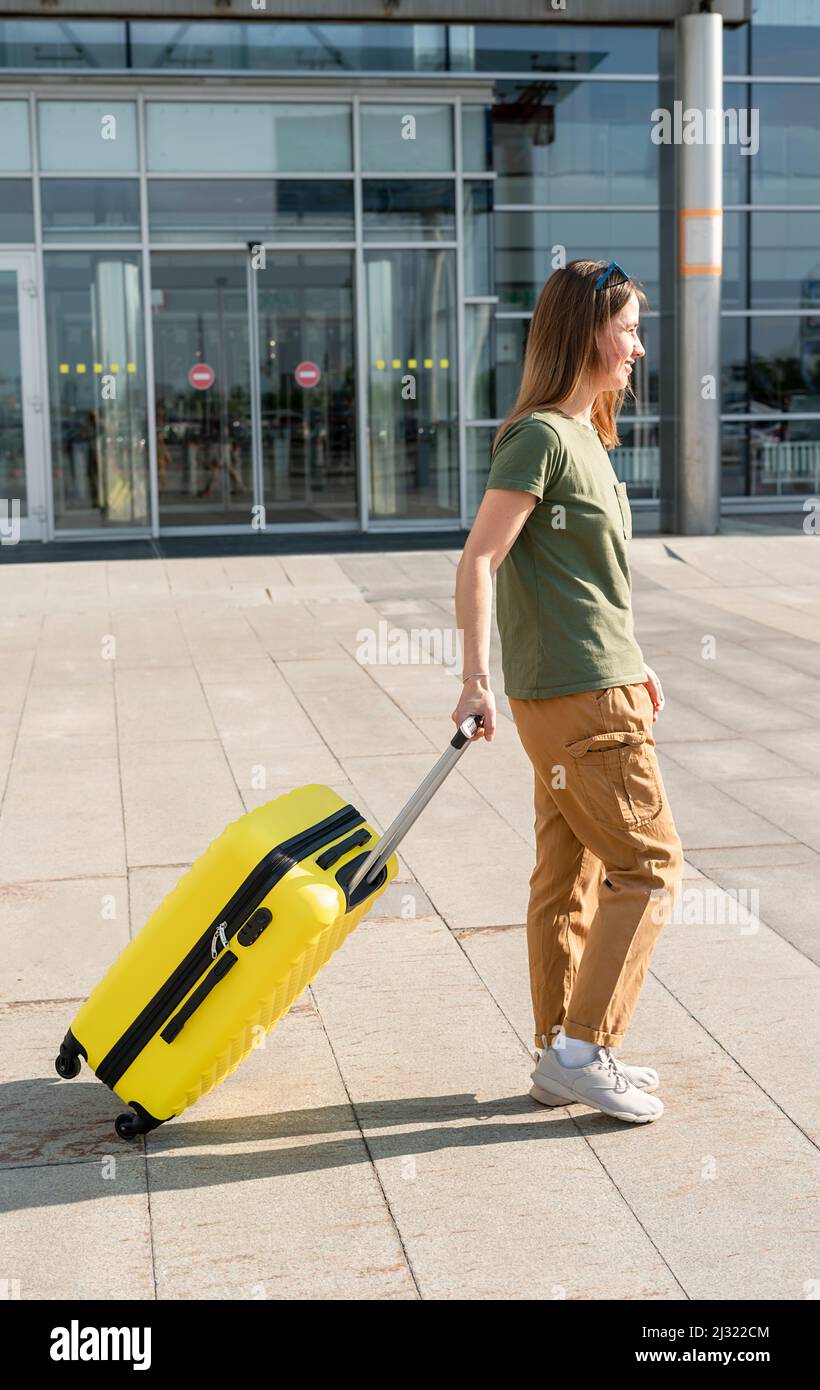Jeune femme voyageur dans des vêtements décontractés portant une valise  jaune à côté de l'entrée de l'aéroport hors du concept de tourisme de vols d 'air voyage un Photo Stock - Alamy