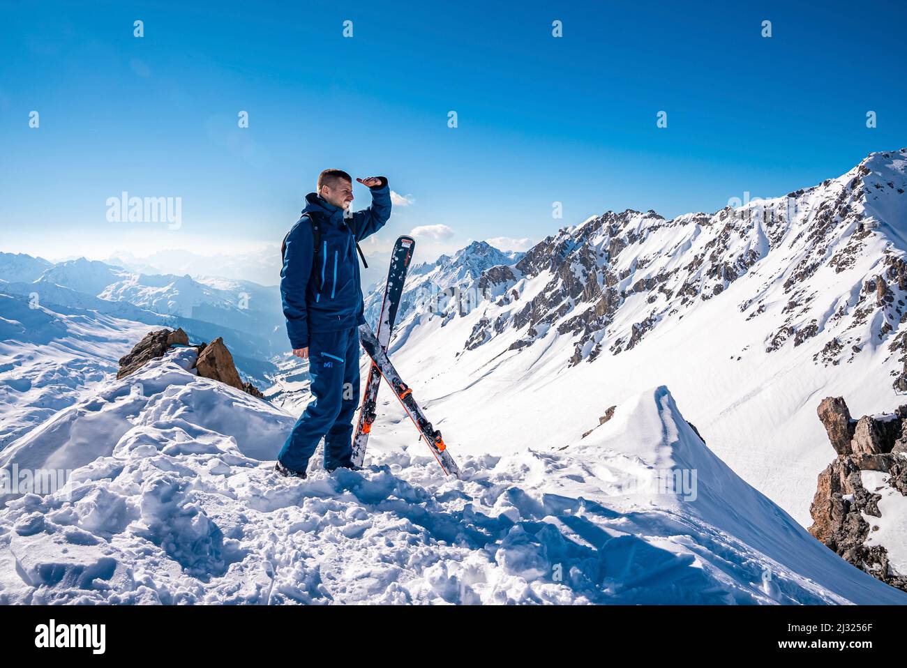 Jeune homme debout à côté de skis sur le sommet de la montagne enneigée le jour ensoleillé Banque D'Images