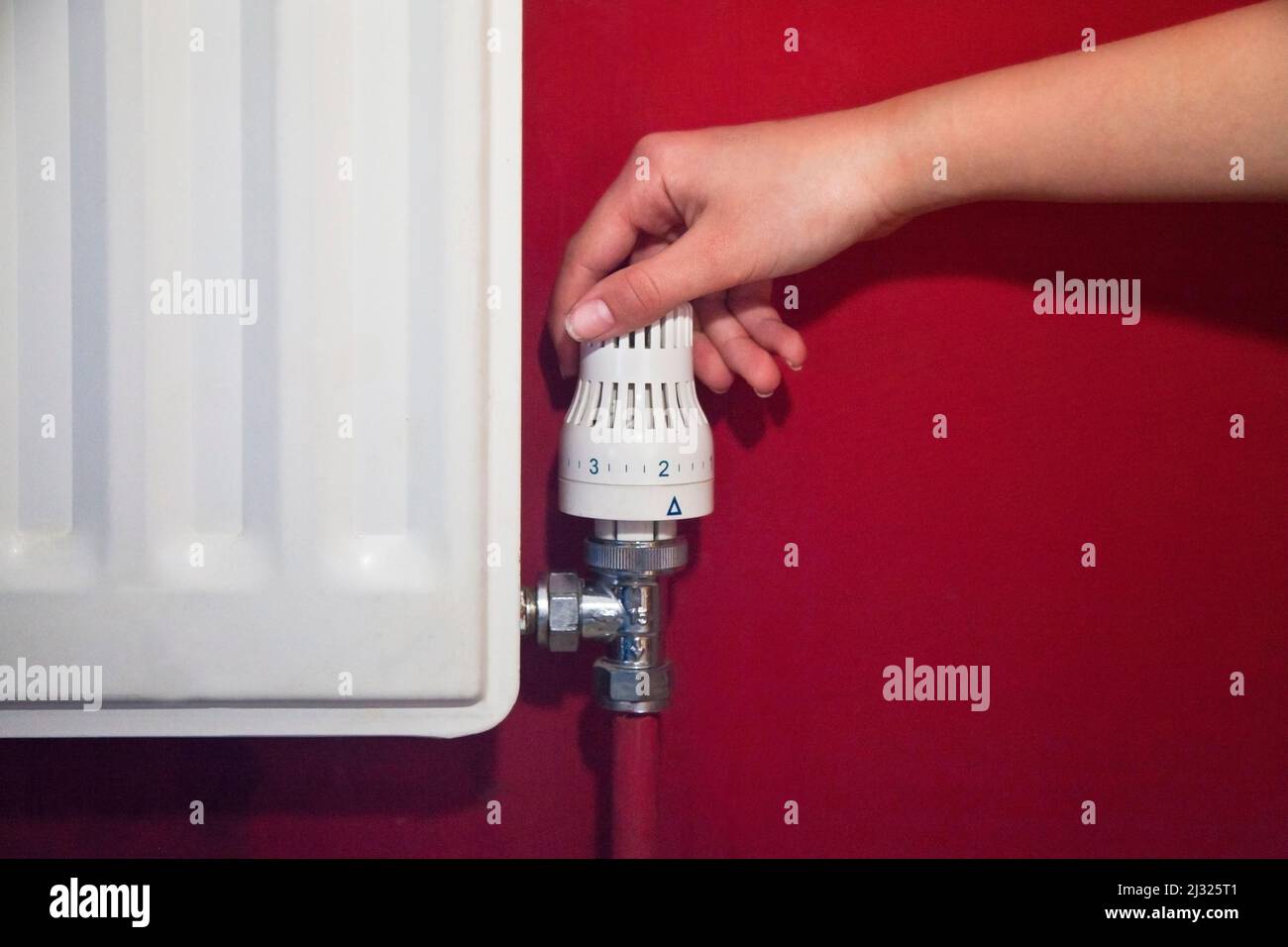 Une main tournant le distributeur du radiateur vers le bas pour économiser l'énergie, sur un mur rouge Banque D'Images