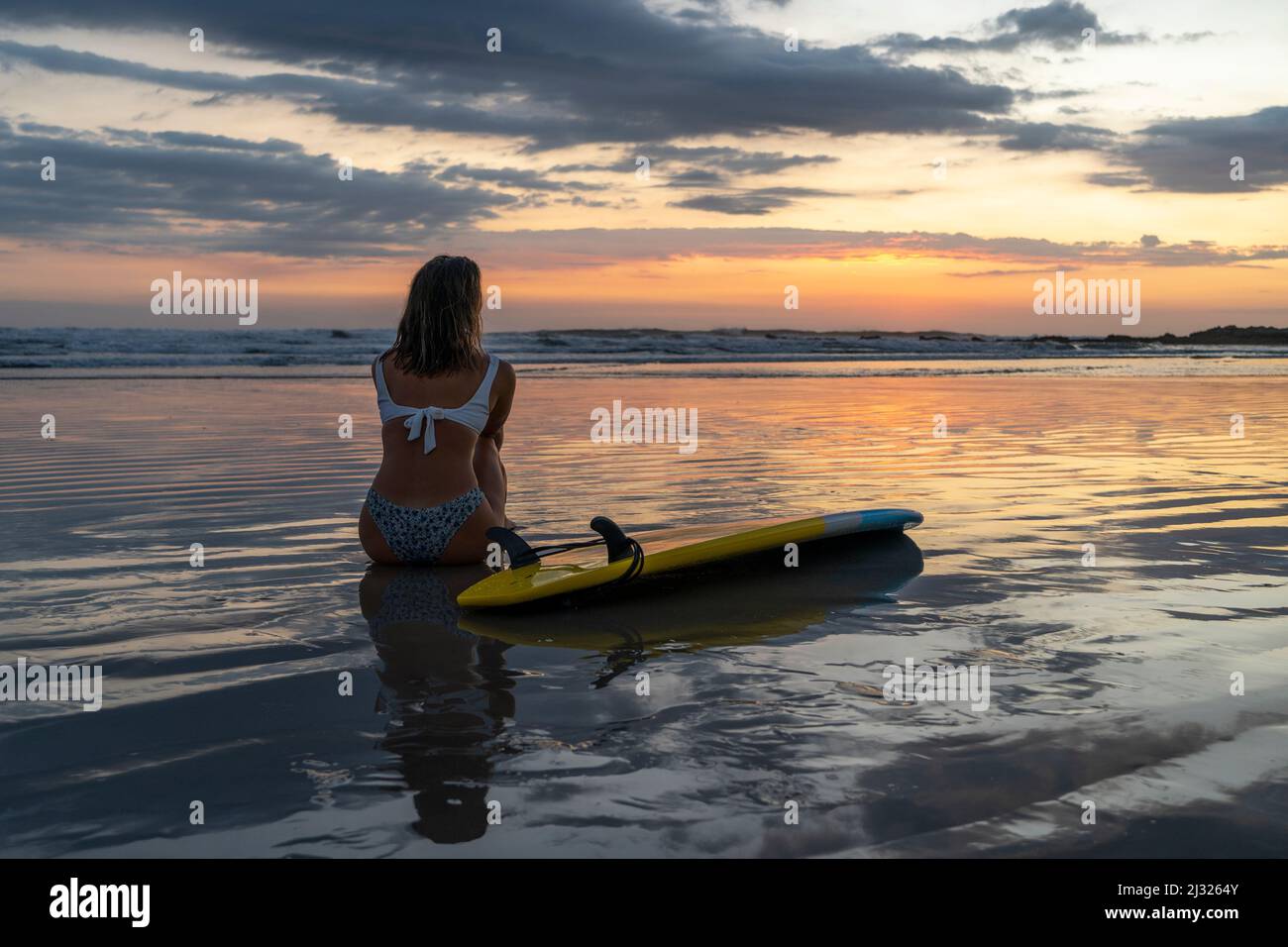 Surfeuse fille avec planche de surf sur la plage au coucher du soleil, belles couleurs à l'heure d'or Banque D'Images