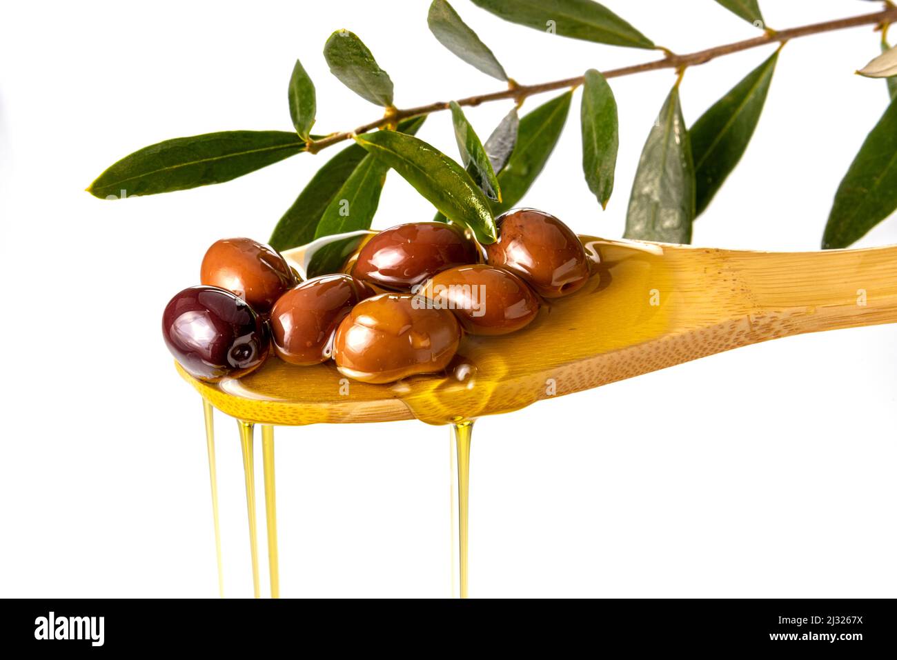 Huile d'olive extra vierge s'écoulant des olives sur une cuillère en bois avec branche de feuille d'olive, isolée sur blanc Banque D'Images