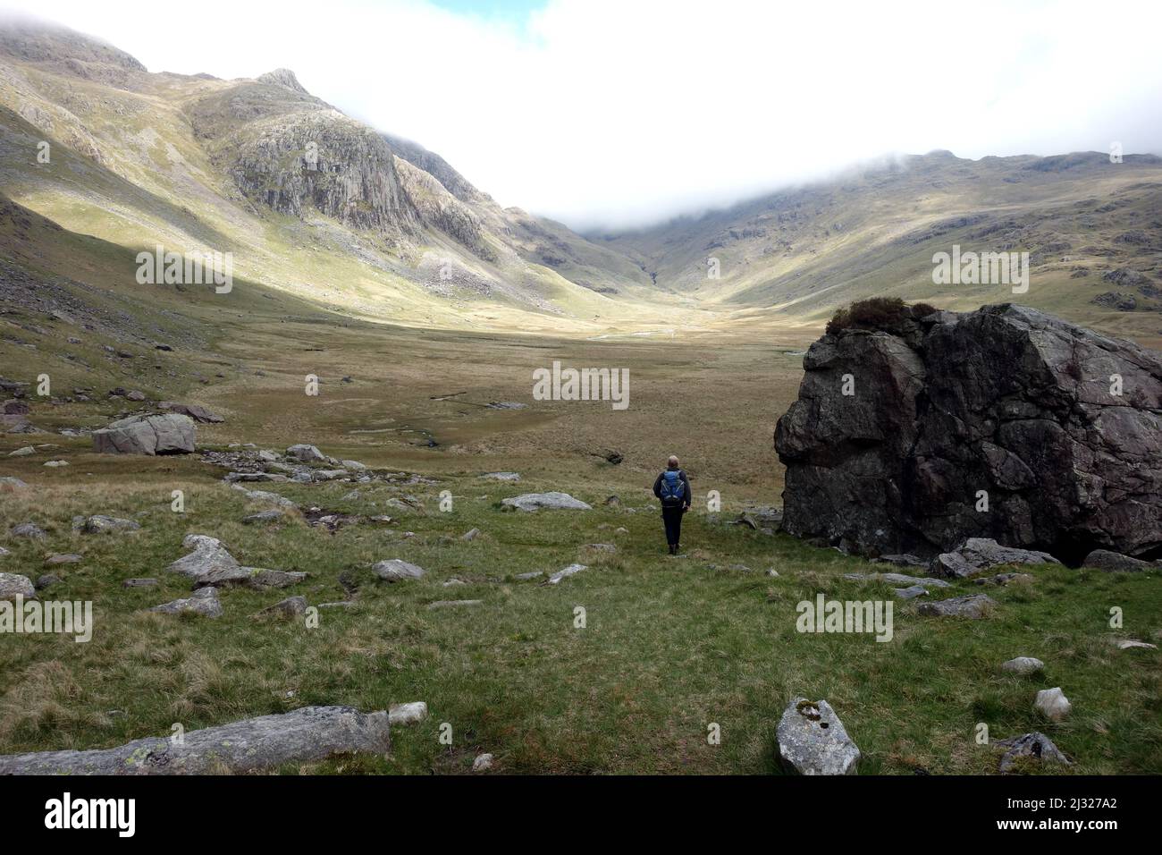 Homme marchant par un énorme Boulder près de River Esk jusqu'à la chaîne de montagnes de Scafell dans la vallée d'Eskdale, Lake District National Park, Cumbria, Angleterre, Royaume-Uni. Banque D'Images