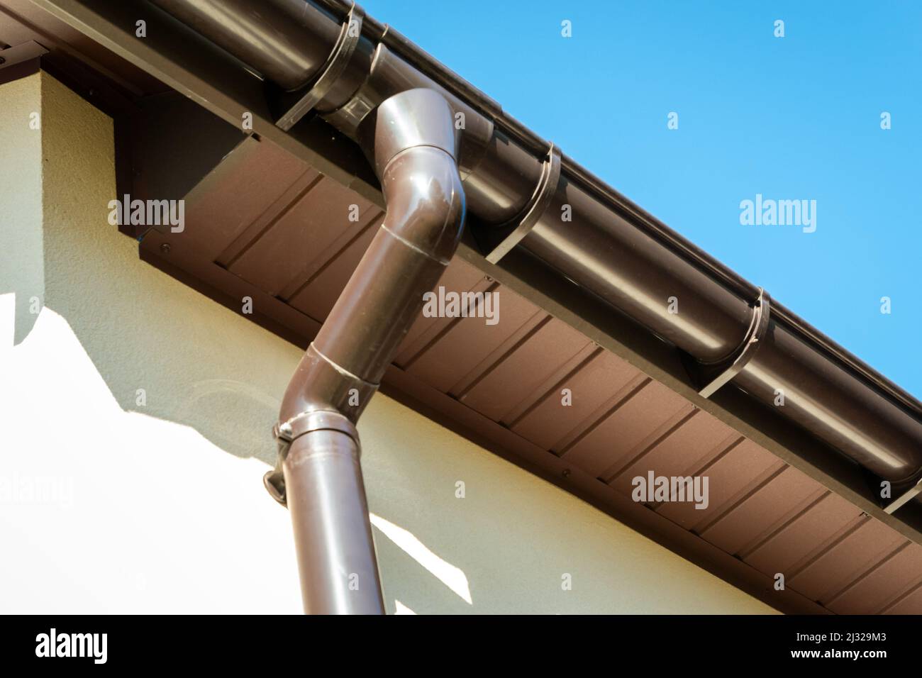 Gouttière en pvc marron reliée au tuyau de descente sur le bord du toit et le ciel. Banque D'Images