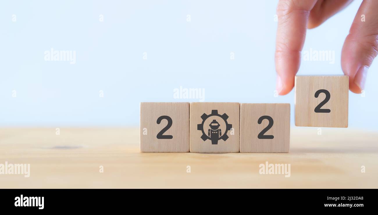 Nouvelle année 2022, concept futuriste et numérique avec technologie robotique. La main tient des cubes en bois avec 2022 lettres et le symbole robot sur le dos blanc Banque D'Images