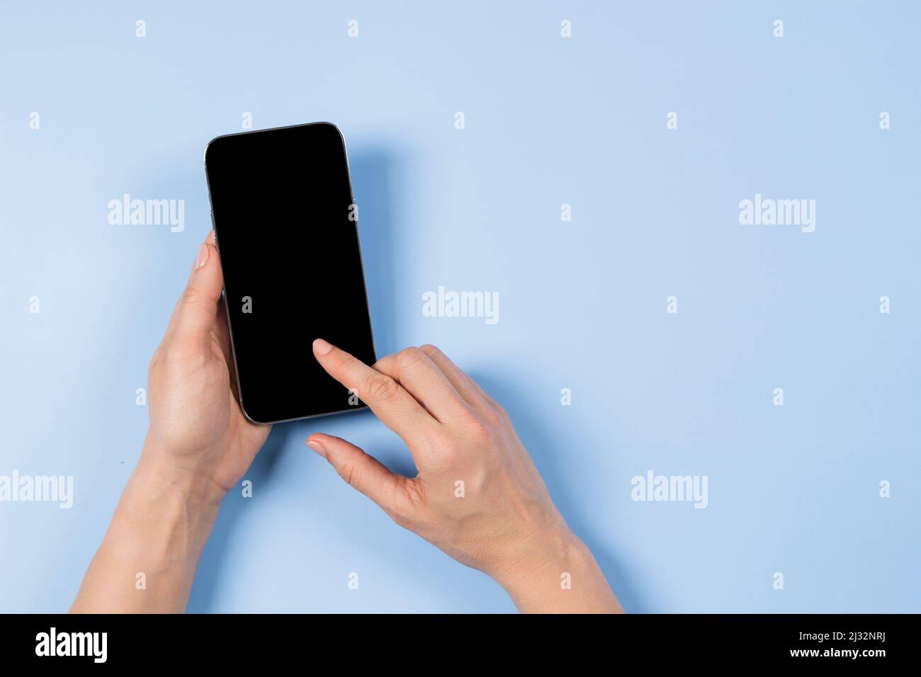 Main féminine touchant l'écran du smartphone et pointant avec l'index sur l'écran vierge du téléphone mobile sur fond bleu clair Banque D'Images