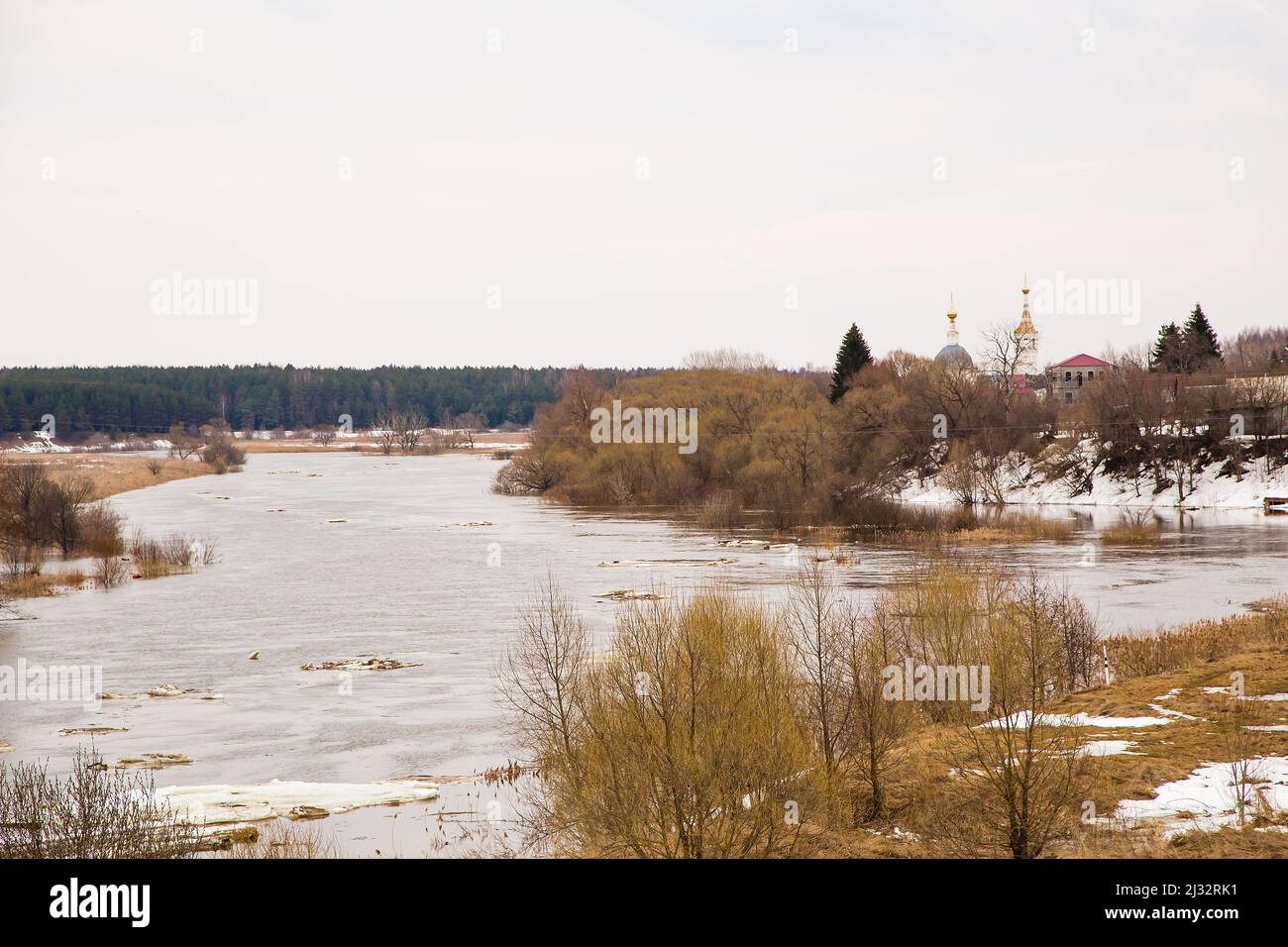 Des morceaux de banquise blanche flottent sur la rivière. Le printemps, la neige fond, l'herbe sèche tout autour, les inondations commencent et la rivière déborde. Jour, temps nuageux, lumière douce et chaude. Banque D'Images