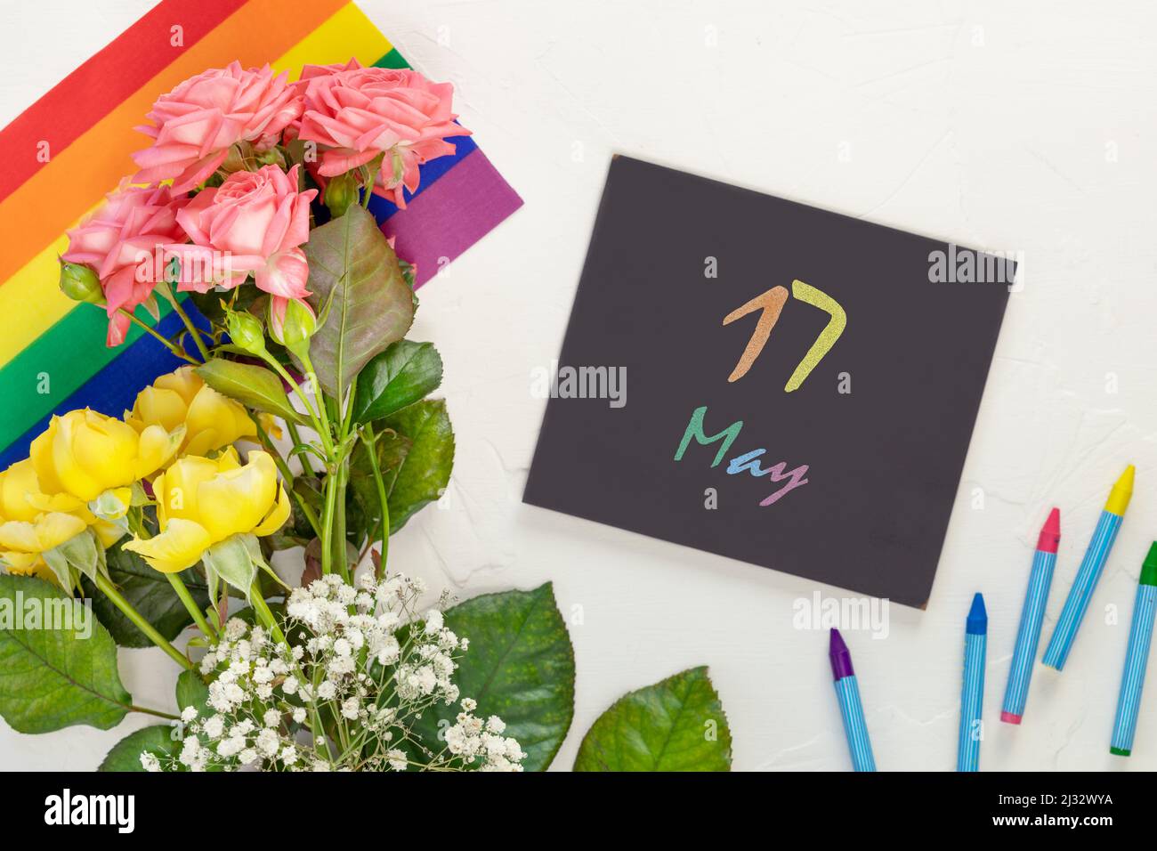Composition LGBT avec roses roses roses roses et jaunes sur un drapeau arc-en-ciel et tableau noir avec inscription le 17 mai et craies sur fond blanc. 17 mai, Interna Banque D'Images