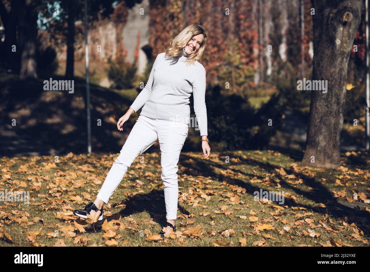 Femme blonde en riant, en profitant de la nature en plein air, en jouant le jour au large de feuilles jaunes dorées mauves. Sur une colline Banque D'Images