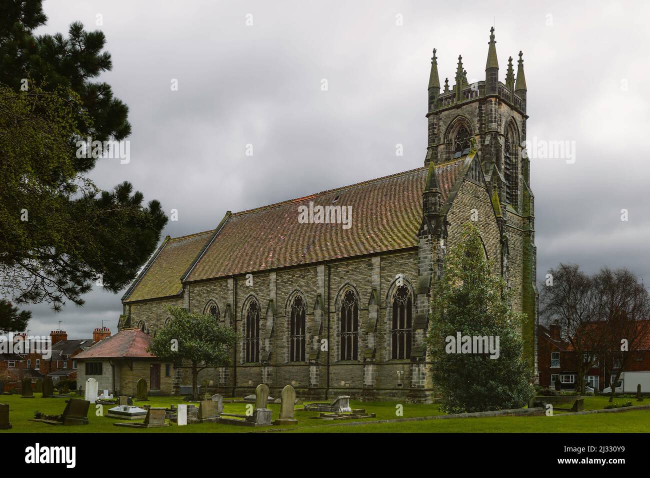 Église Saint-Nicolas avec vue sur les pierres tombales et flanquée de pelouses et d'arbres dans un ciel nuageux sur un morninbg printanier à Beverley, Yorkshire, Royaume-Uni. Banque D'Images