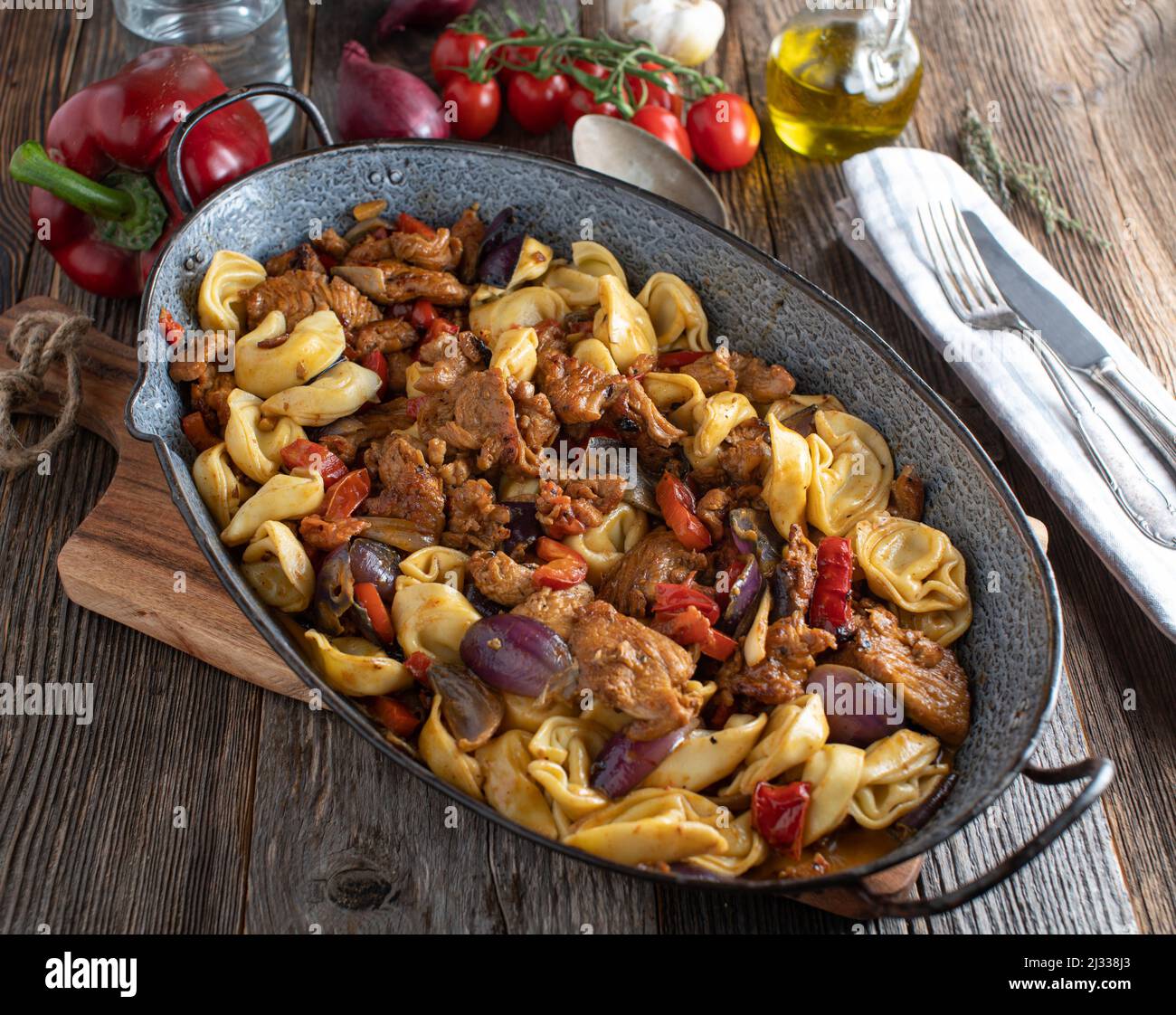 Dans une rôtissoire sur une table en bois, faire cuire la viande de porc frite avec les légumes, la sauce et les tortellini Banque D'Images