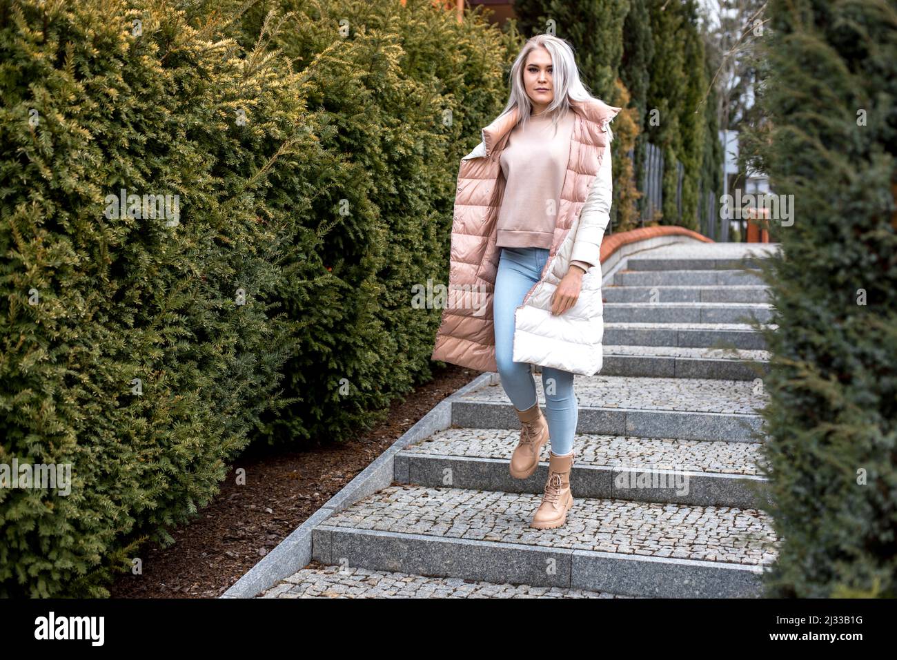 Portrait de jeune femme magnifique sérieuse avec de longs cheveux gris avec maquillage debout en blanc, rose veste réversible. Banque D'Images