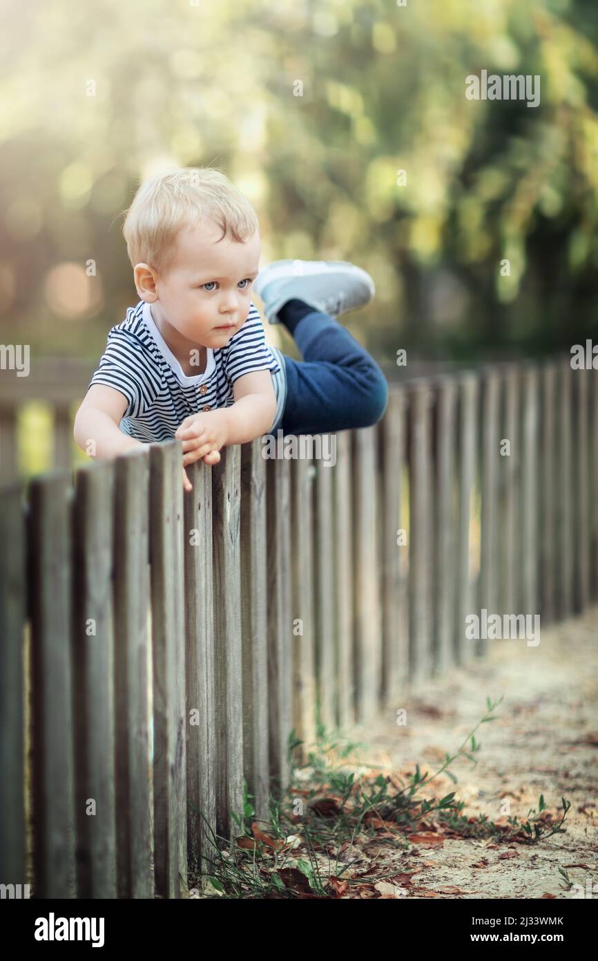 Petit garçon grimpant sur une clôture en bois dans un jardin. Enfants jouant dans la nature concept Banque D'Images