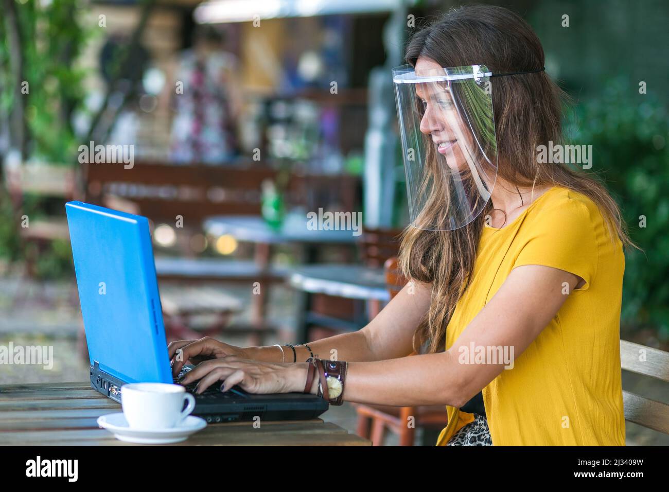 femme assise dans un café vide portant une visière de protection et travaillant sur un ordinateur portable Banque D'Images