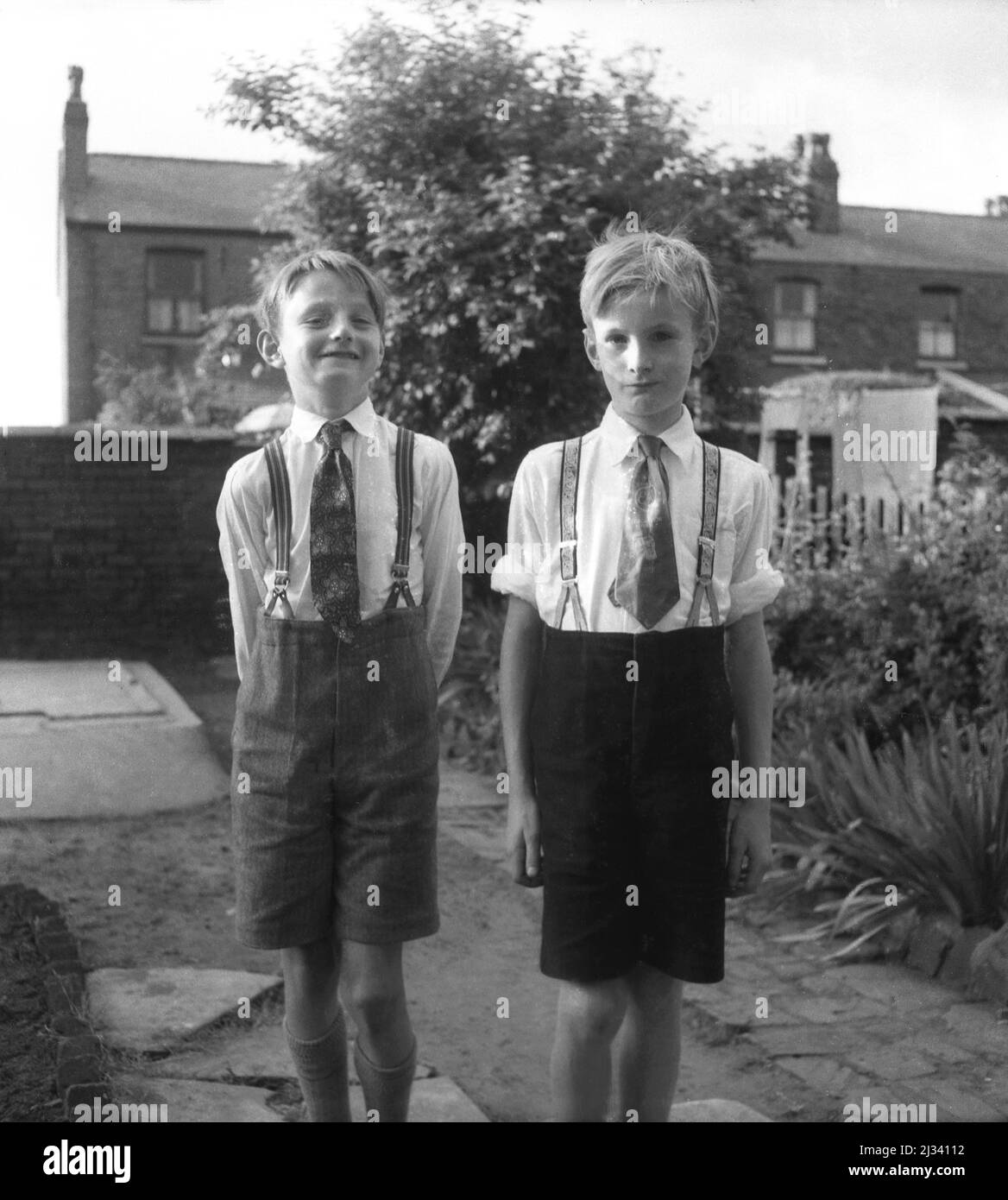 1960s, historique, deux jeunes garçons, frères, debout à l'extérieur dans  un jardin à l'arrière pour leur photo, portant une chemise et des cravates  et un pantalon court, tenu par des bretelles, Stockport,