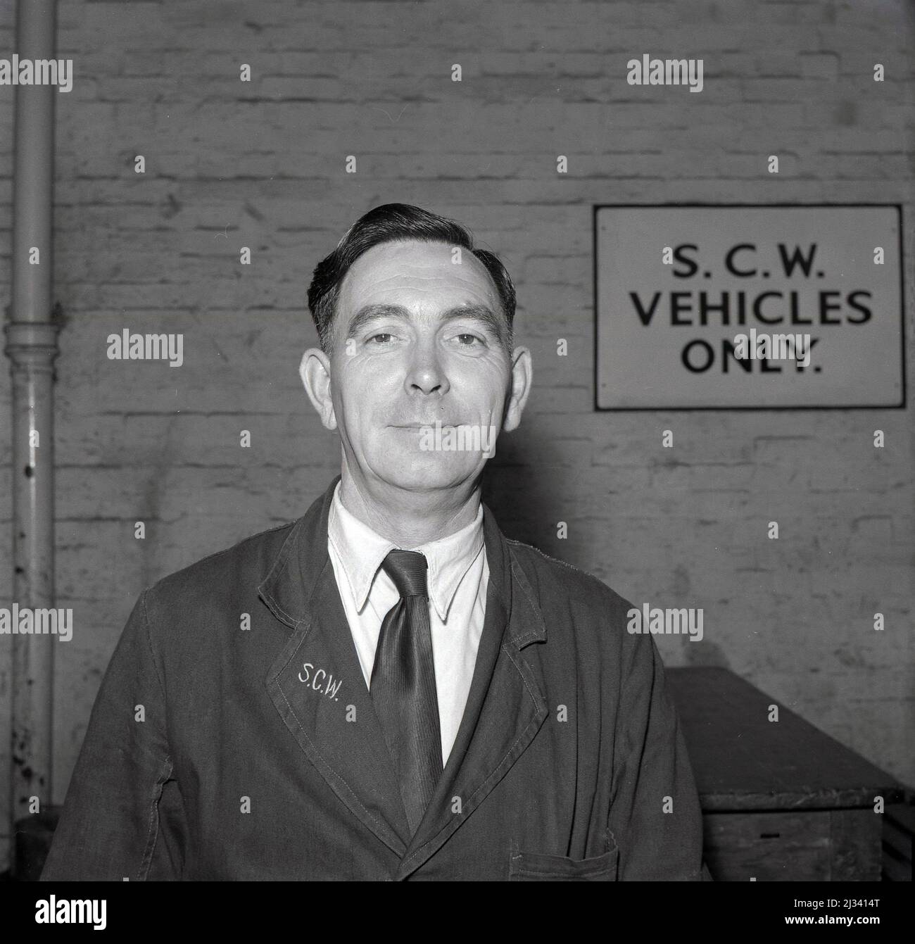 1950s, historique, un directeur de travaux de la compagnie d'acier du pays de Galles, portant un ensemble de lin de marque d'entreprise sur une chemise et une cravate, Abbey Works, Port Talbot, pays de Galles. Un panneau sur le mur indique uniquement les véhicules S.C.W. Banque D'Images