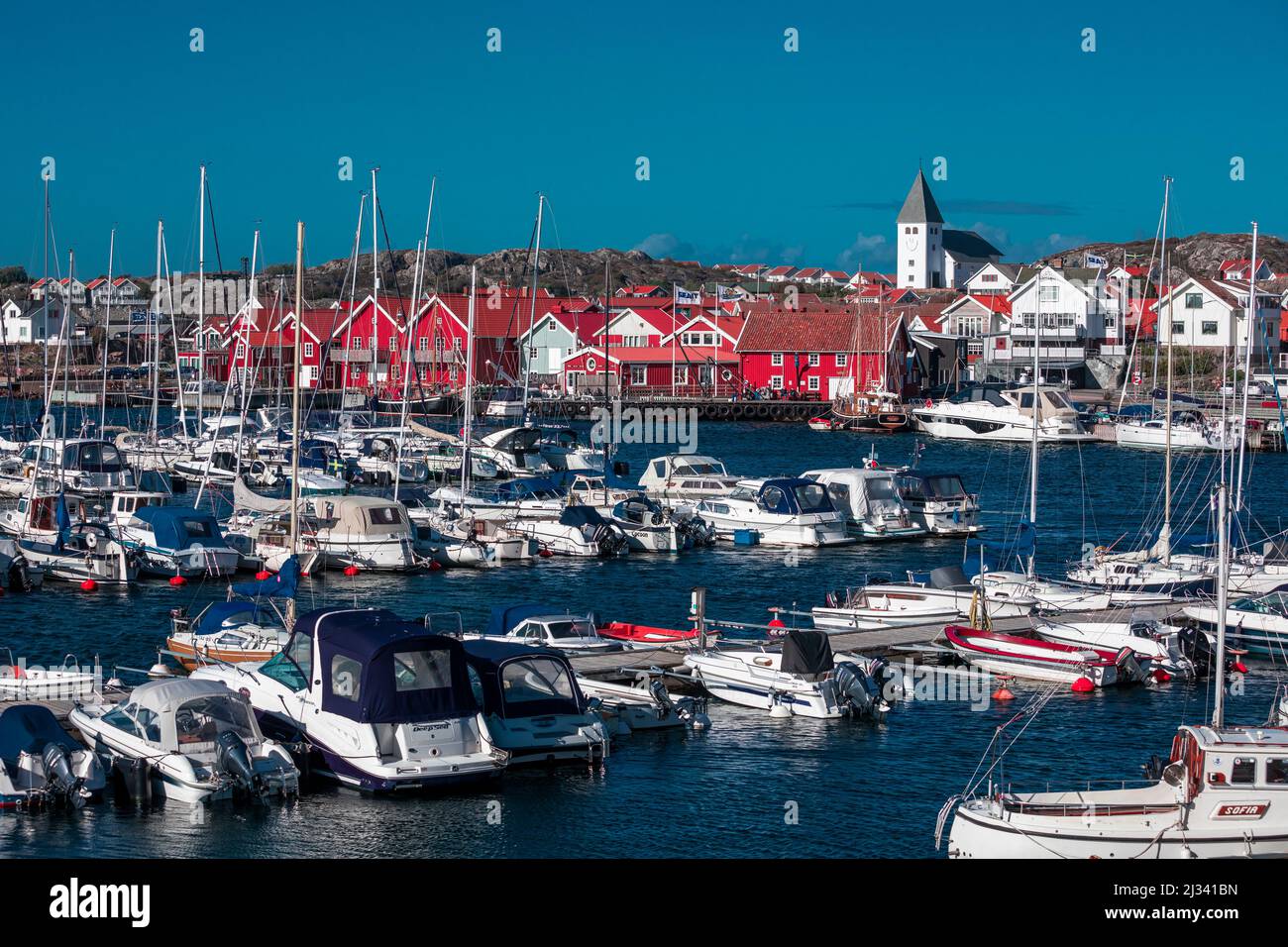 Port et maisons rouges avec église dans le village de Skärhamn sur l'archipel de Tjörn sur la côte ouest de la Suède, ciel bleu avec soleil Banque D'Images