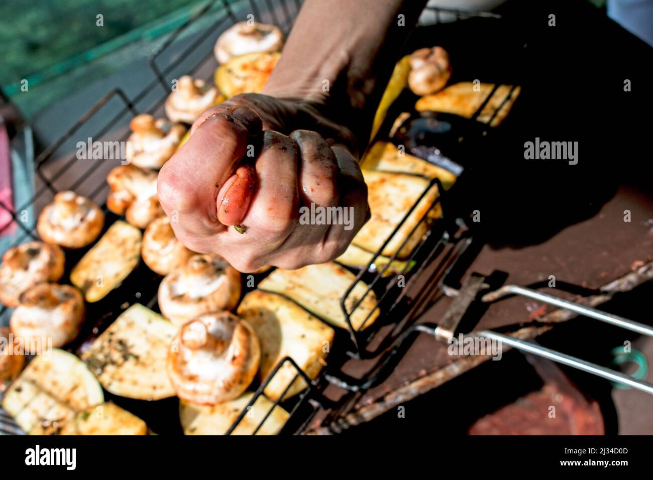 Légumes grillés. Humour. La main d'une femme montre un museau. Griller pour un pique-nique. Nourriture sur un feu ouvert. Courgettes, aubergines et champignons. Légumes frais Banque D'Images