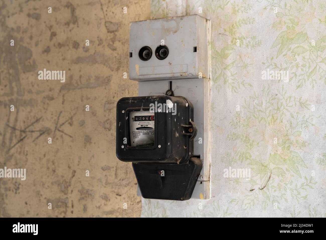 Ancien compteur électrique sur un mur dans un bâtiment abandonné. Équipement électrique pour mesurer la consommation électrique à des fins de comptabilité. Ancien papier peint vintage. Banque D'Images