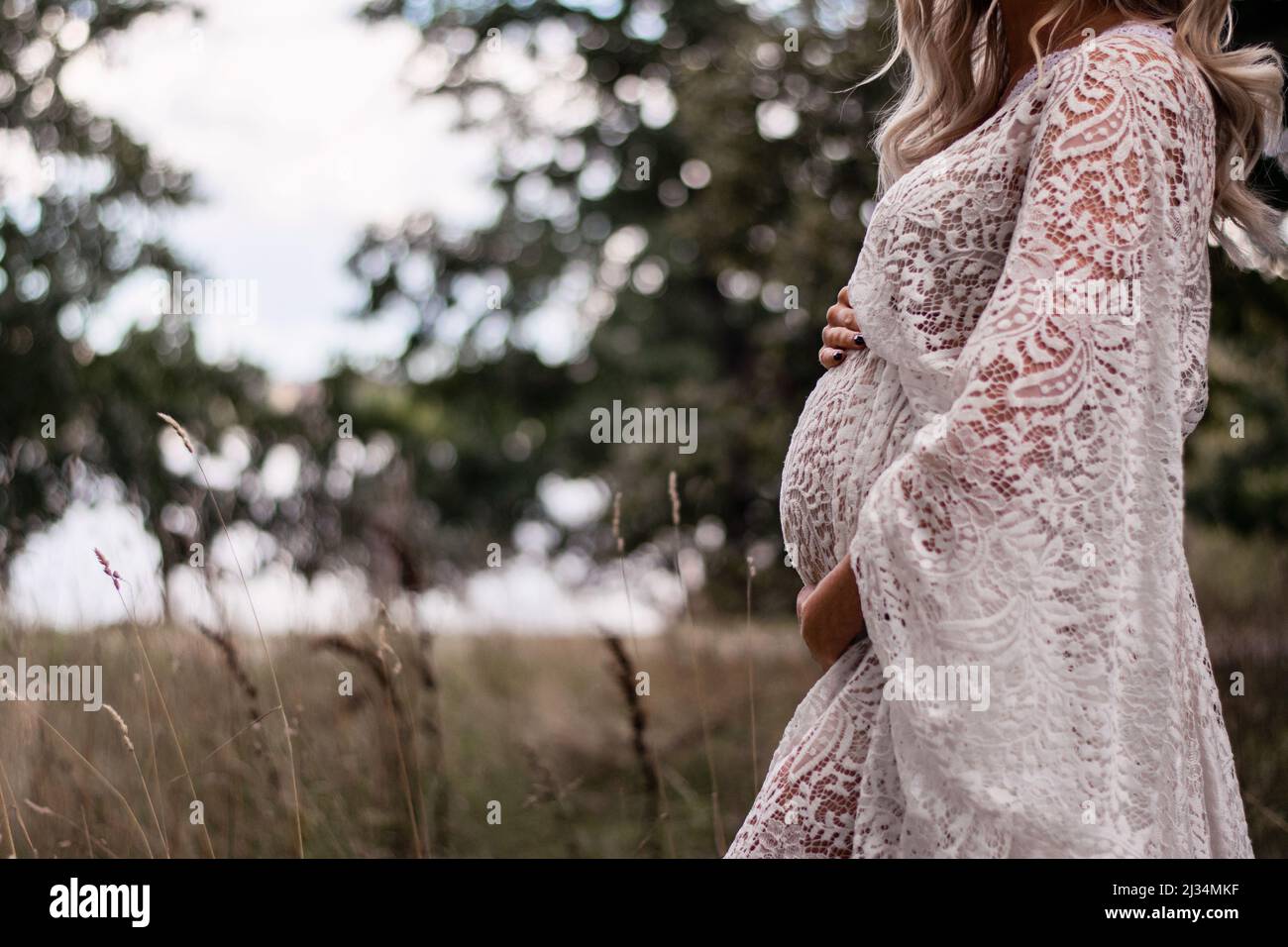 Femme enceinte aux cheveux longs blonds dans la forêt, portant une robe en dentelle boho. Belle robe et s'attendant à une femme à l'extérieur dans la nature. Banque D'Images