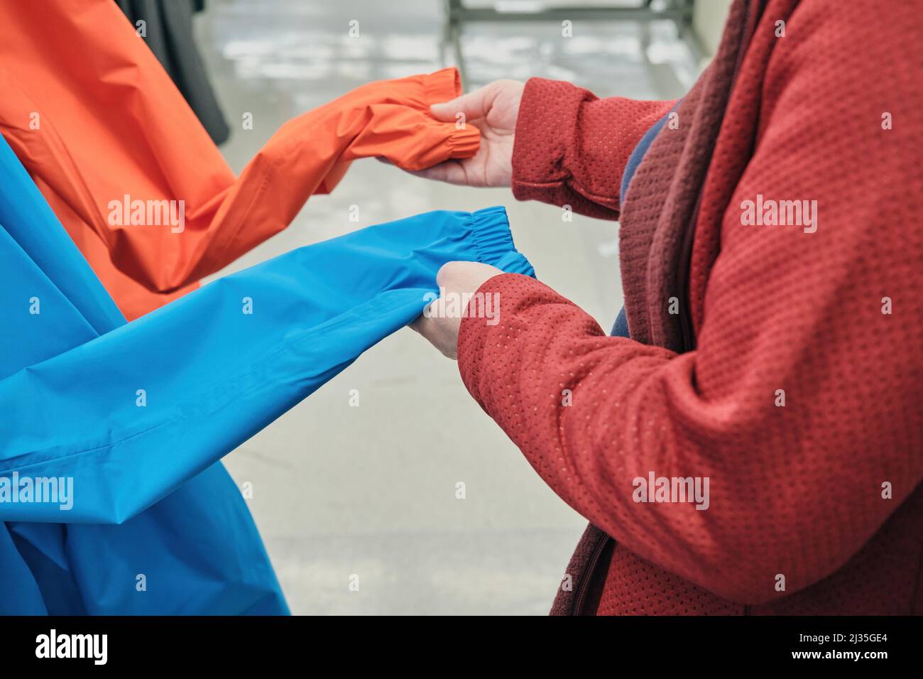 La femme en masque contre le virus choisit un coupe-vent bleu et rouge en magasin pour acheter Banque D'Images