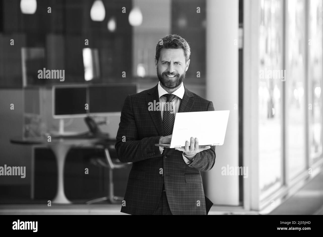 Homme d'affaires tenant son ordinateur portable en costume sur le fond du bureau. Banque D'Images