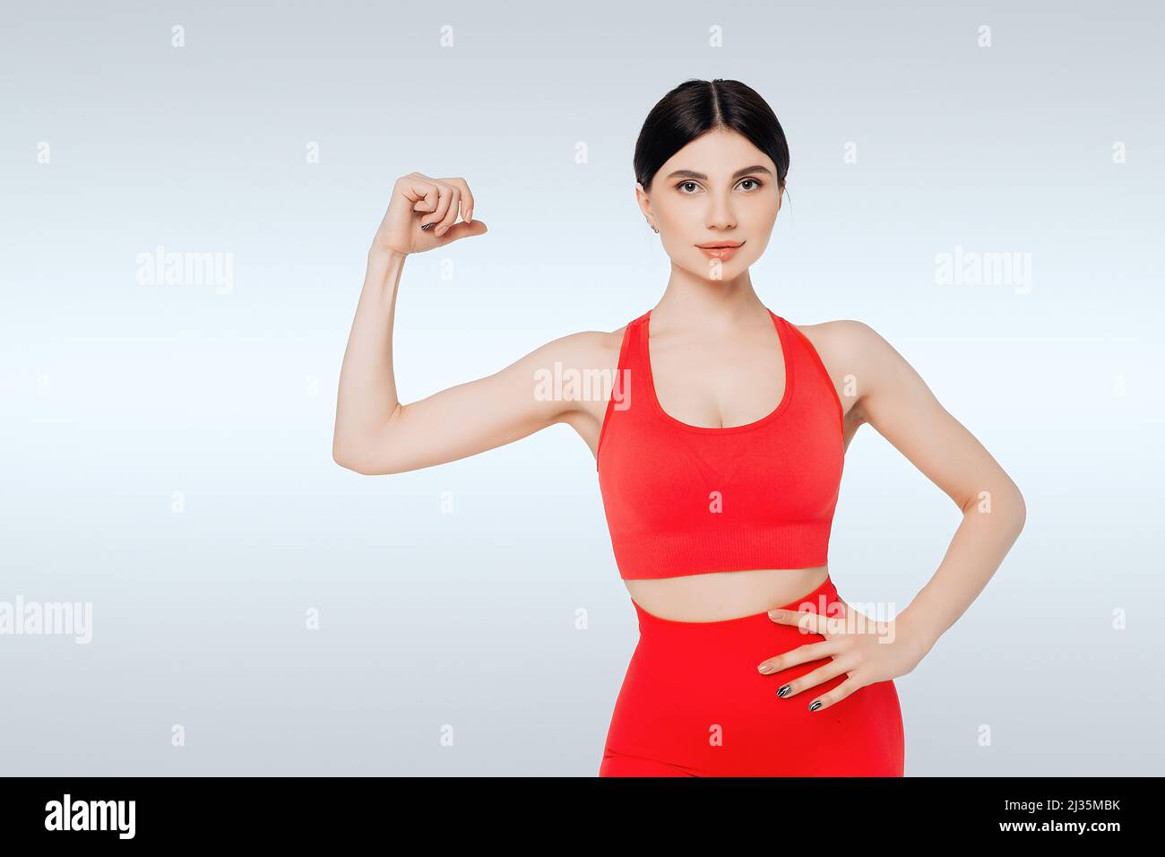 Portrait d'une belle fille portant des vêtements de sport rouges montrant son biceps. Concept de fitness, de bien-être et de force. Banque D'Images