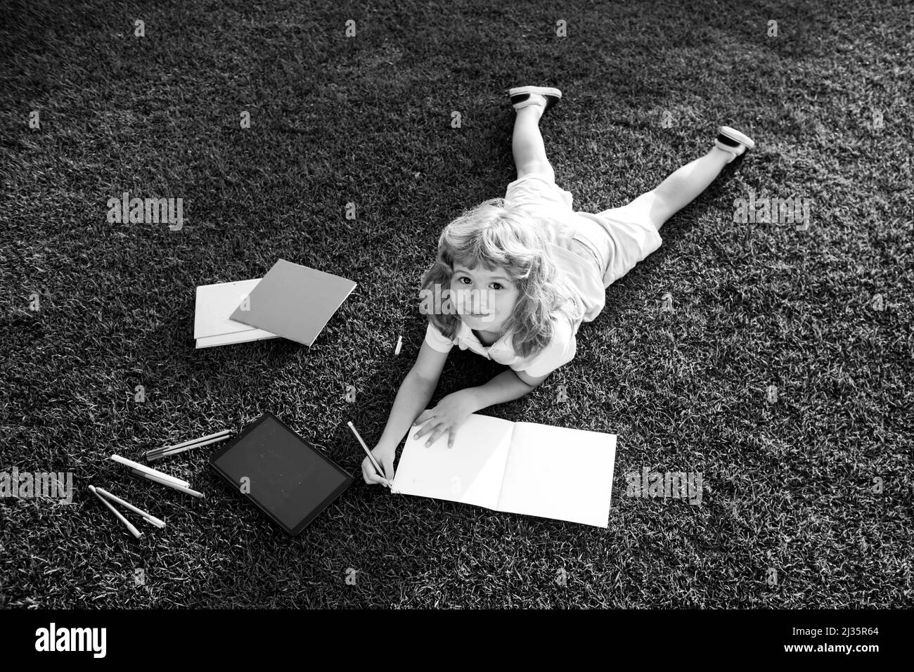 Enfant garçon lisant le livre d'intérêt et écrivant sur le carnet dans le jardin.L'été s'amuser.Adorable garçon allongé sur l'herbe lisant un livre pour enfants. Banque D'Images