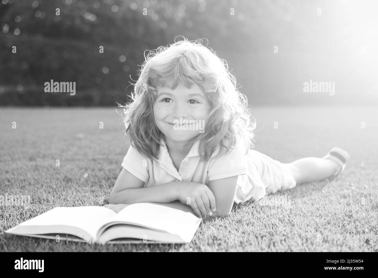 Enfants intelligents.Mignon garçon lisant un livre sur l'herbe.Un enfant lit un livre dans le parc d'été. Banque D'Images