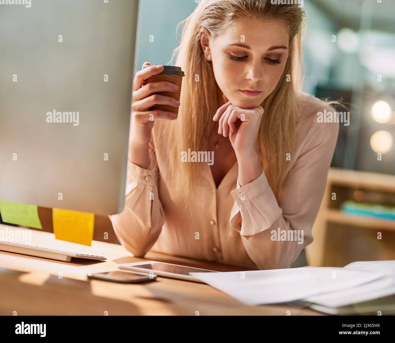 Travailler en profondeur sa pause-café. Photo d'une jeune femme d'affaires assise à son bureau pour lire des documents. Banque D'Images