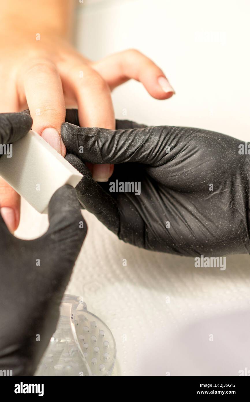 Gros plan des mains caucasiennes d'un manucuriste professionnel sont en dépôt les ongles d'une jeune femme. Jeune femme caucasienne recevant une manucure par une esthéticienne avec une lime à ongles dans un salon de manucure Banque D'Images