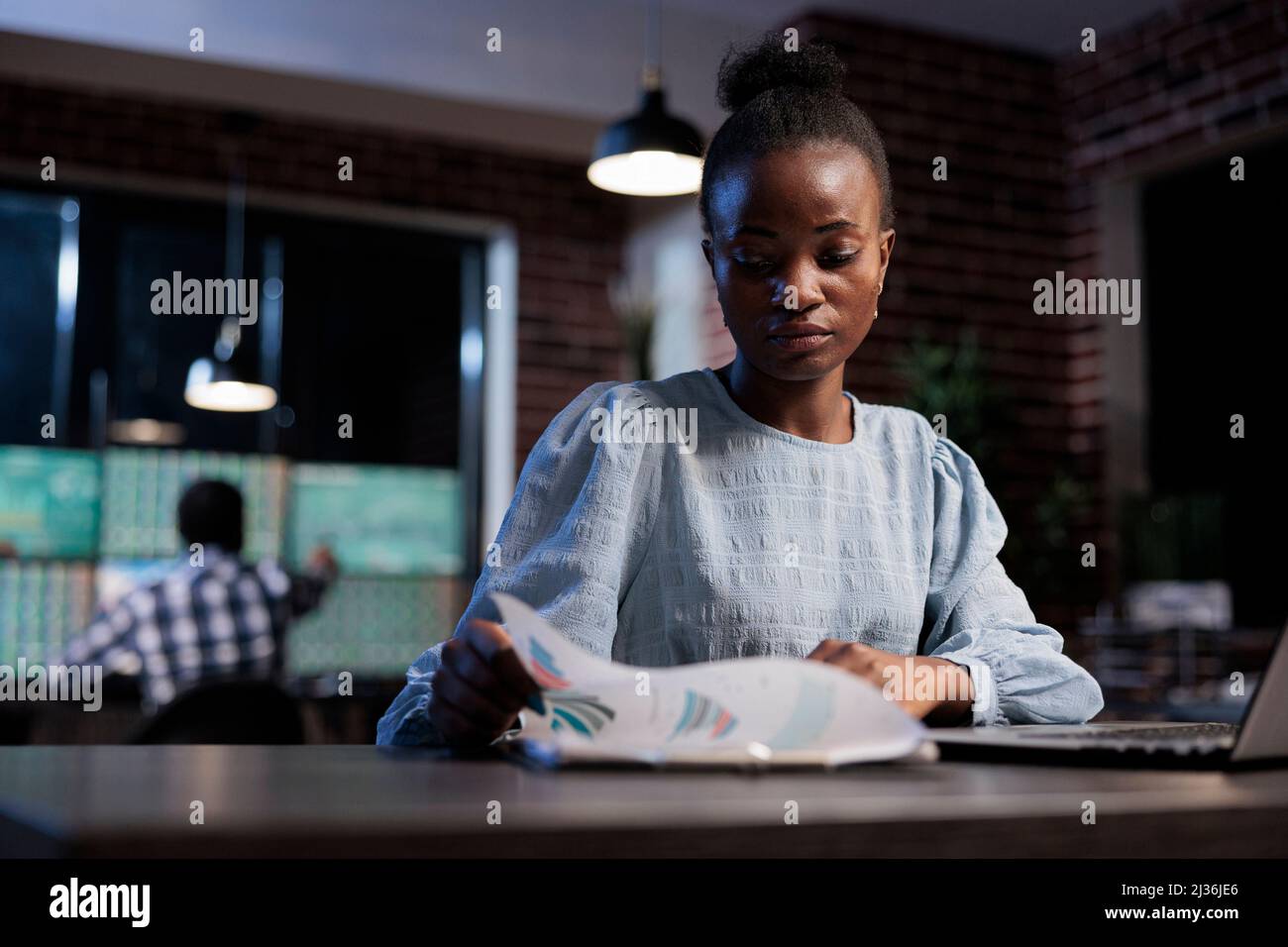 Forex stock Agent analysant les graphiques financiers tout en regardant la paperboard. Le représentant des ventes de la société de financement examine la documentation sur les tendances du marché pendant qu'il est assis au bureau la nuit. Banque D'Images