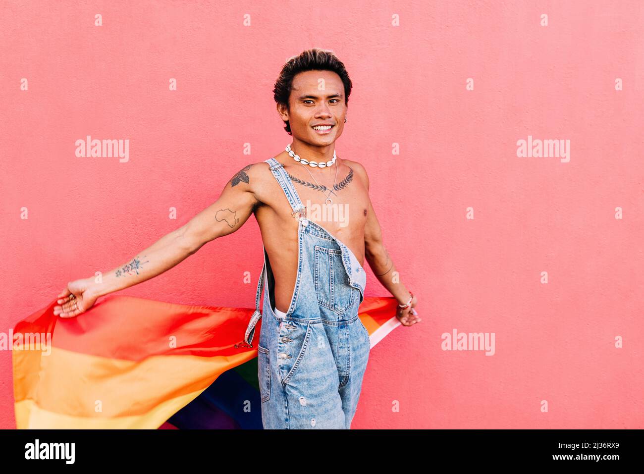 Jeune homme en combinaison denim portant un drapeau arc-en-ciel à l'extérieur Banque D'Images