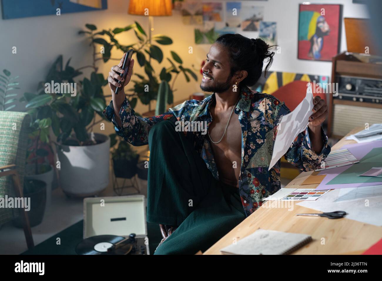 Portrait d'un jeune artiste joyeux ou d'un designer d'origine indienne assis sur une chaise et portant un selfie sur un appareil photo de smartphone Banque D'Images