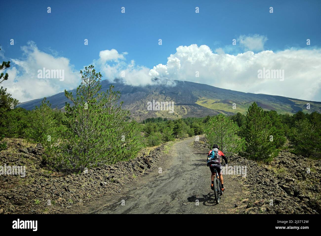 ADRANO, PARC DE L'ETNA, SICILE, ITALIE - 25 AOÛT 2018 : un motard de montagne roule sur une route de terre le long des pentes menant à la ligne des arbres Banque D'Images