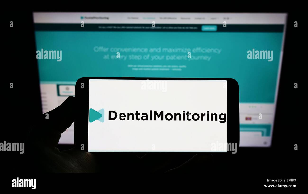 Personne portant un smartphone avec le logo de la société de santé française Dental Monitoring SAS sur l'écran devant le site. Mise au point sur l'affichage du téléphone. Banque D'Images