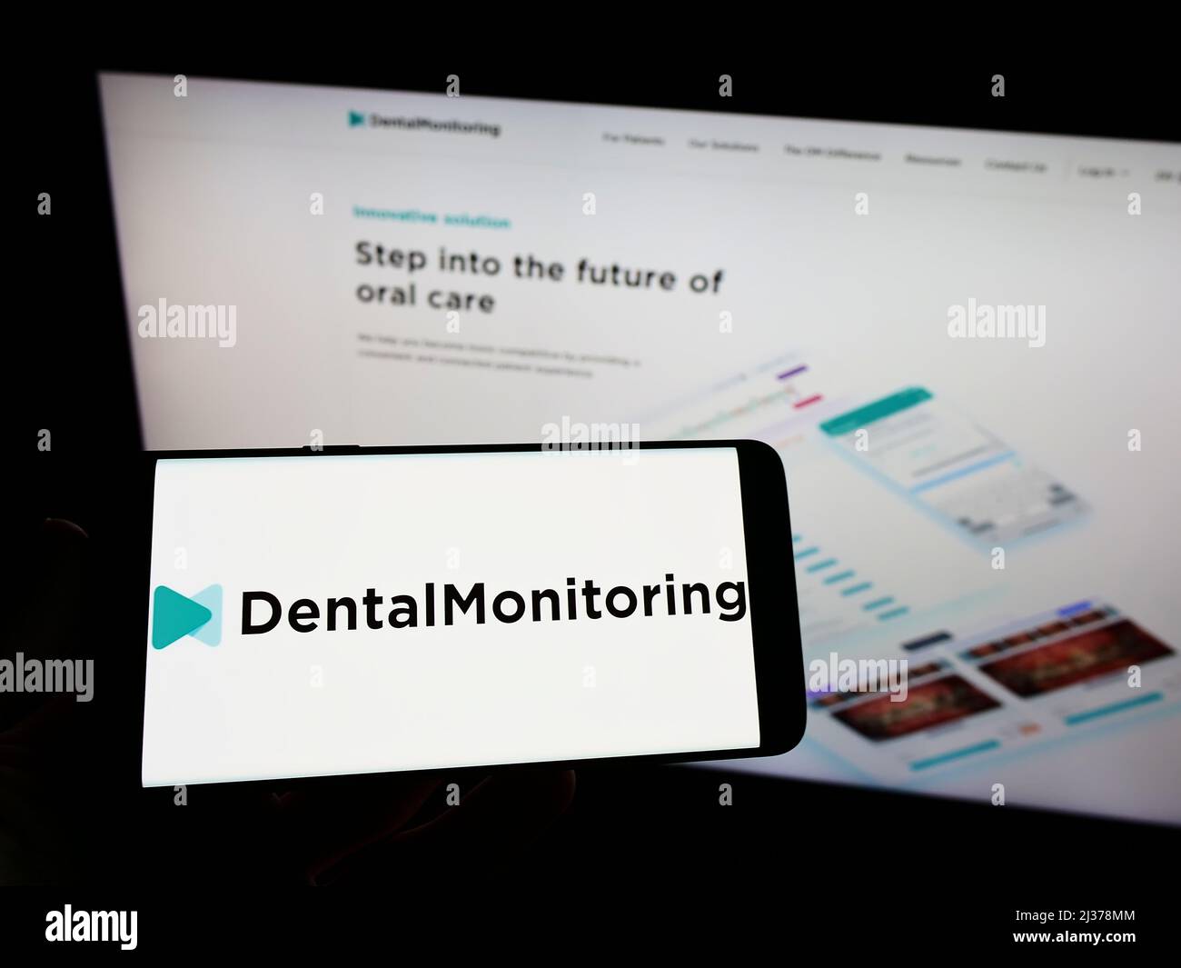 Personne tenant un téléphone portable avec le logo de la société française de santé Dental Monitoring SAS sur l'écran en face de la page web. Mise au point sur l'affichage du téléphone. Banque D'Images