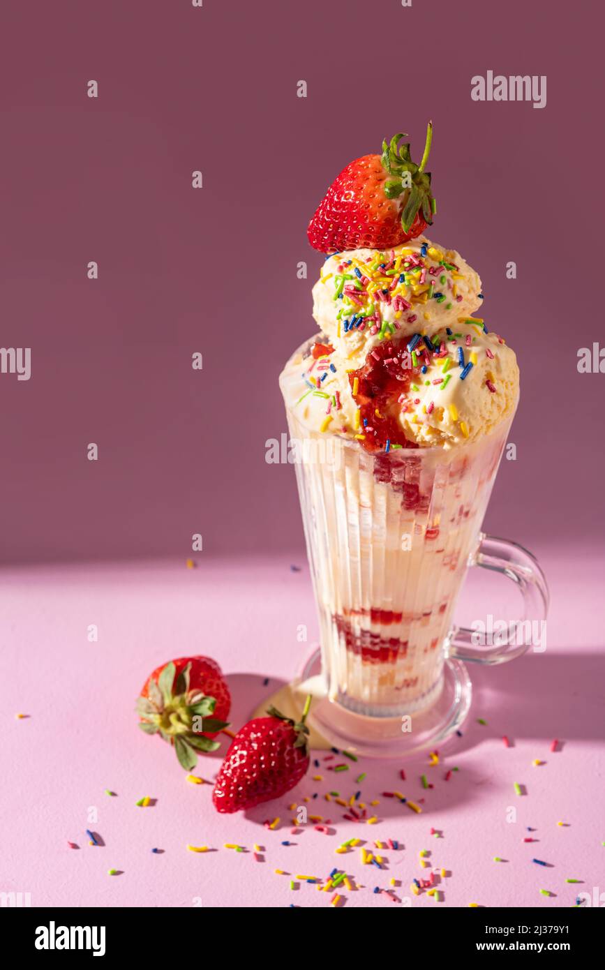 Milkshake à la crème glacée à la vanille garni de fraises fraîches et de saupoudrées colorées sur fond rose Banque D'Images Milkshake à la crème glacée à la vanille garni de fraises fraîches et de saupoudrées colorées sur fond rose Banque D'Images