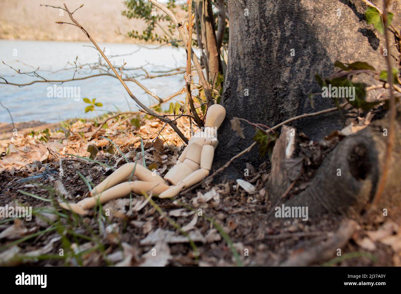 Mannequin en bois assis devant le corps de l'arbre, marionnette en bois faire une sieste sur la forêt, vue latérale, détente et refroidissement, concept d'automne Banque D'Images