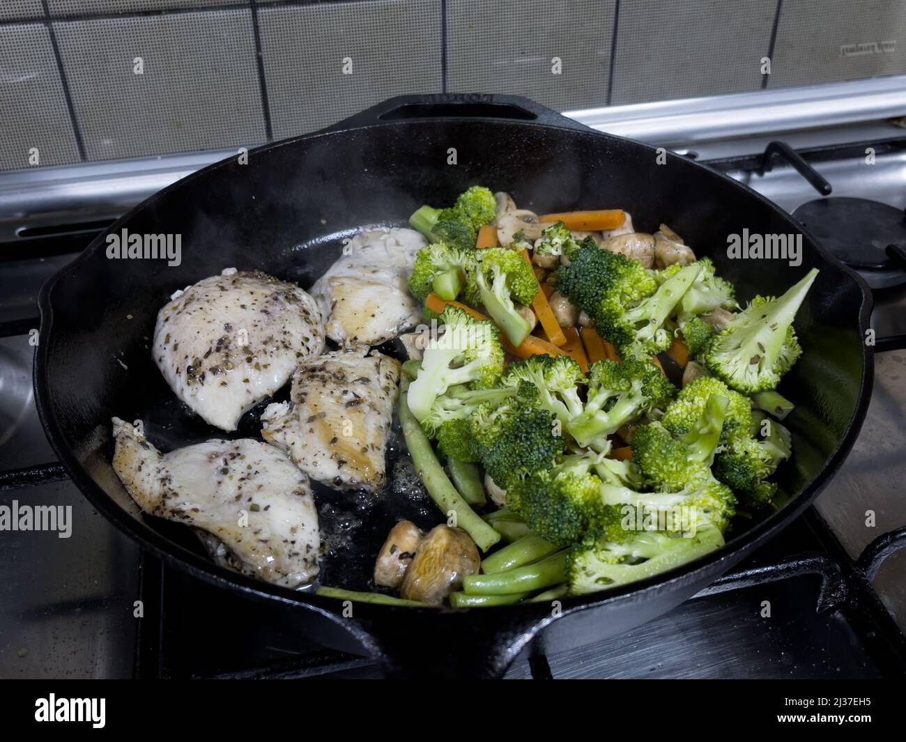 Un mélange de légumes et de poulet mélangé avec des herbes, du poivre et du sel cuit sur une poêle en fonte. Banque D'Images