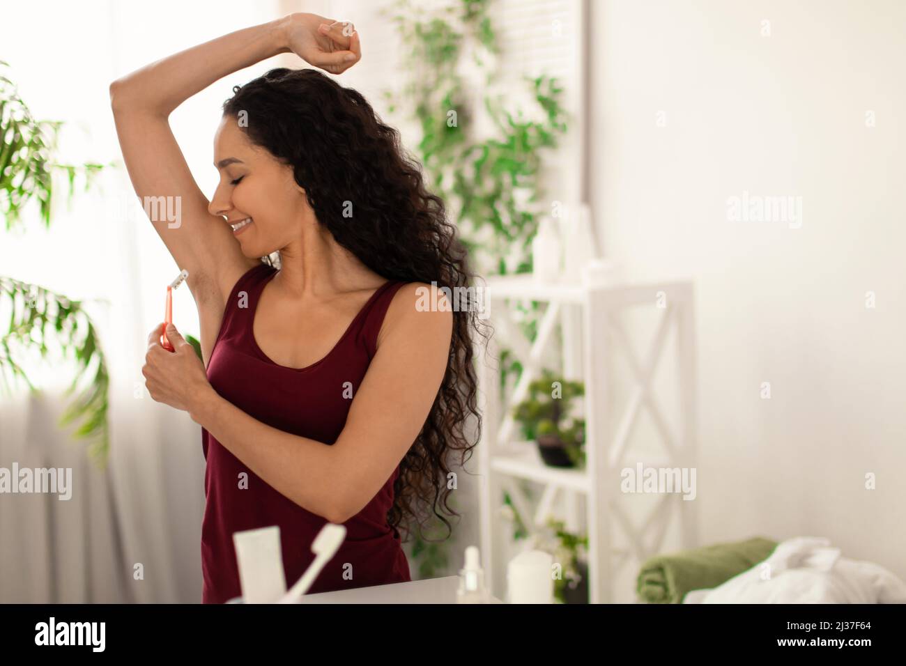 Bonne jeune femme se raser les aisselles avec un rasoir, éliminant les  poils indésirables devant le miroir à la maison, espace libre Photo Stock -  Alamy