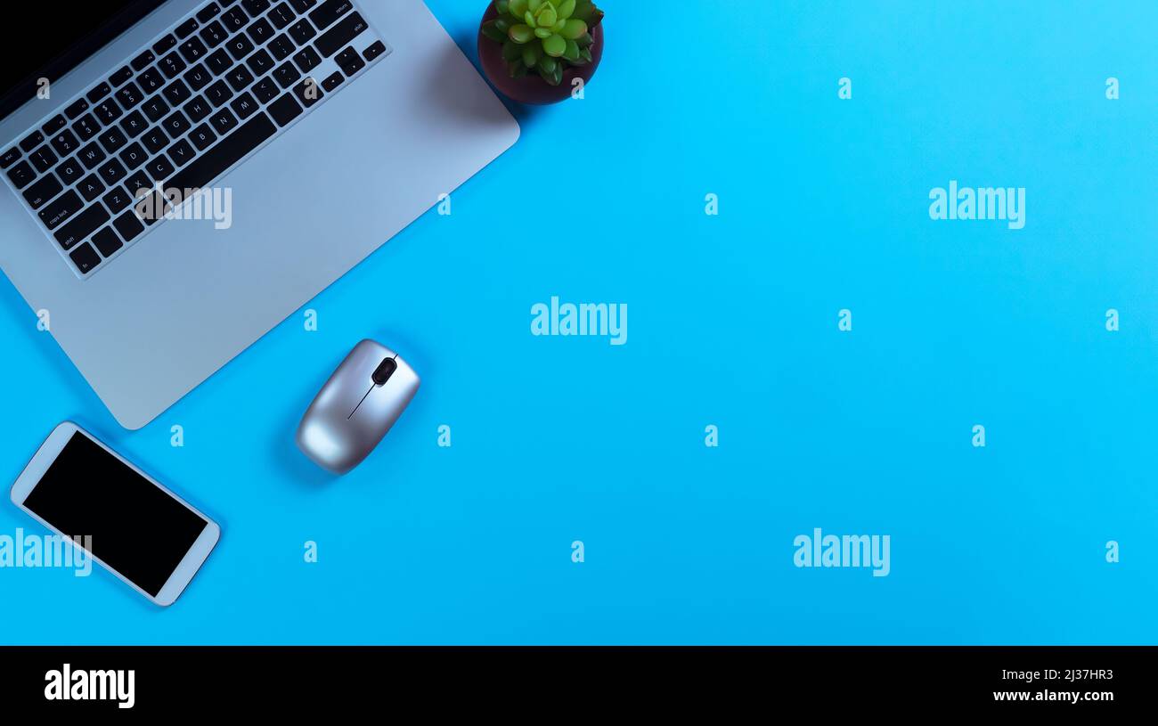 Table de bureau bleue avec ordinateur portable, usine, smartphone et souris. Vue de dessus avec espace de copie en mode de mise en page en mode sans barre. Concept d'école ou de travail. Banque D'Images