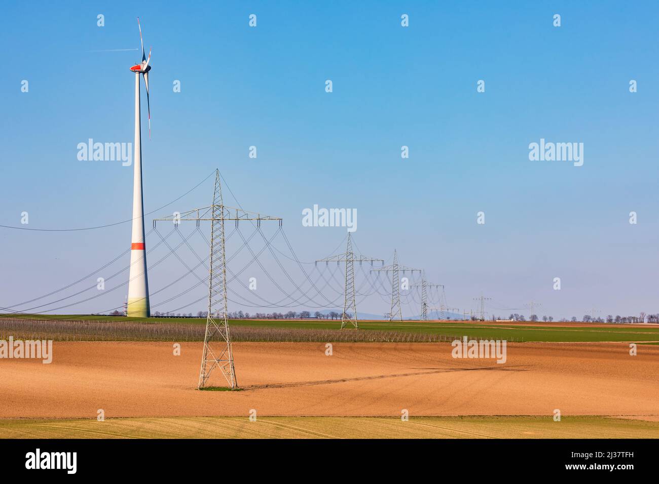 Plusieurs pylônes d'électricité dominent le paysage rural avec une énorme tour d'éolienne en arrière-plan Banque D'Images