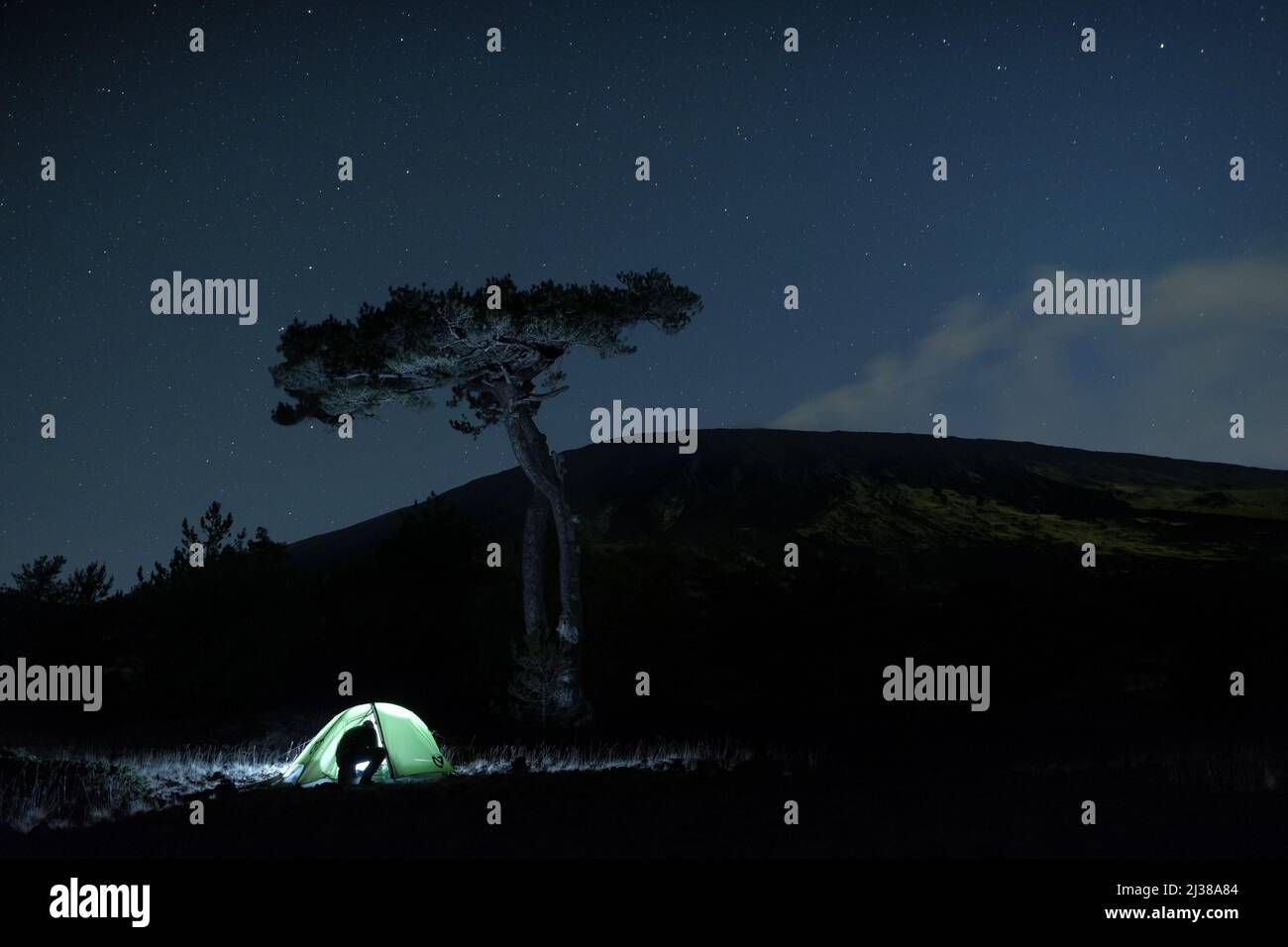 PARC DE L'ETNA, SICILE - 22 OCTOBRE 2017 : silhouette d'un homme entrant dans la tente illuminée sous un grand pin, en arrière-plan le profil du mont de l'Etna Banque D'Images