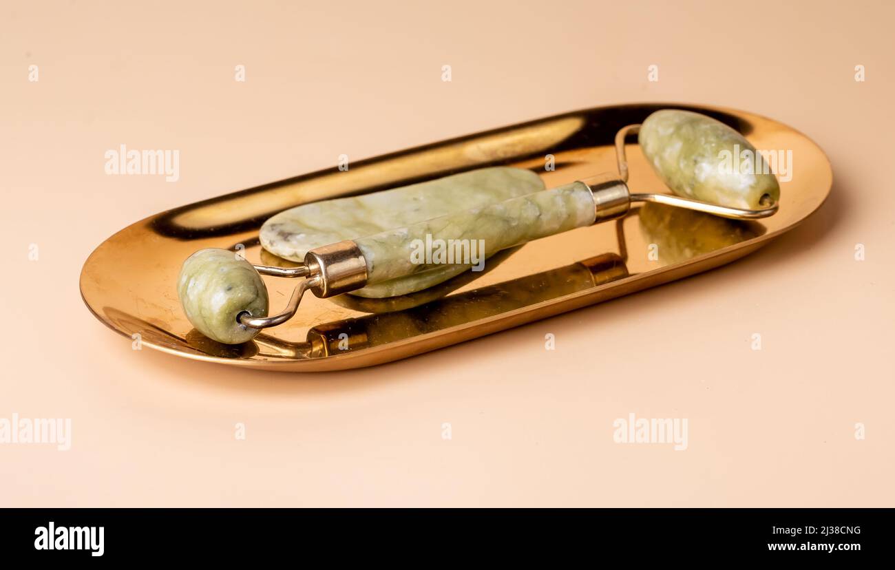 Outils de jade de massage Gua Sha. Grattoir et rouleau sur support doré. Levage, virage et traitement anti-âge. Concept beauté et détente. Photo de haute qualité Banque D'Images